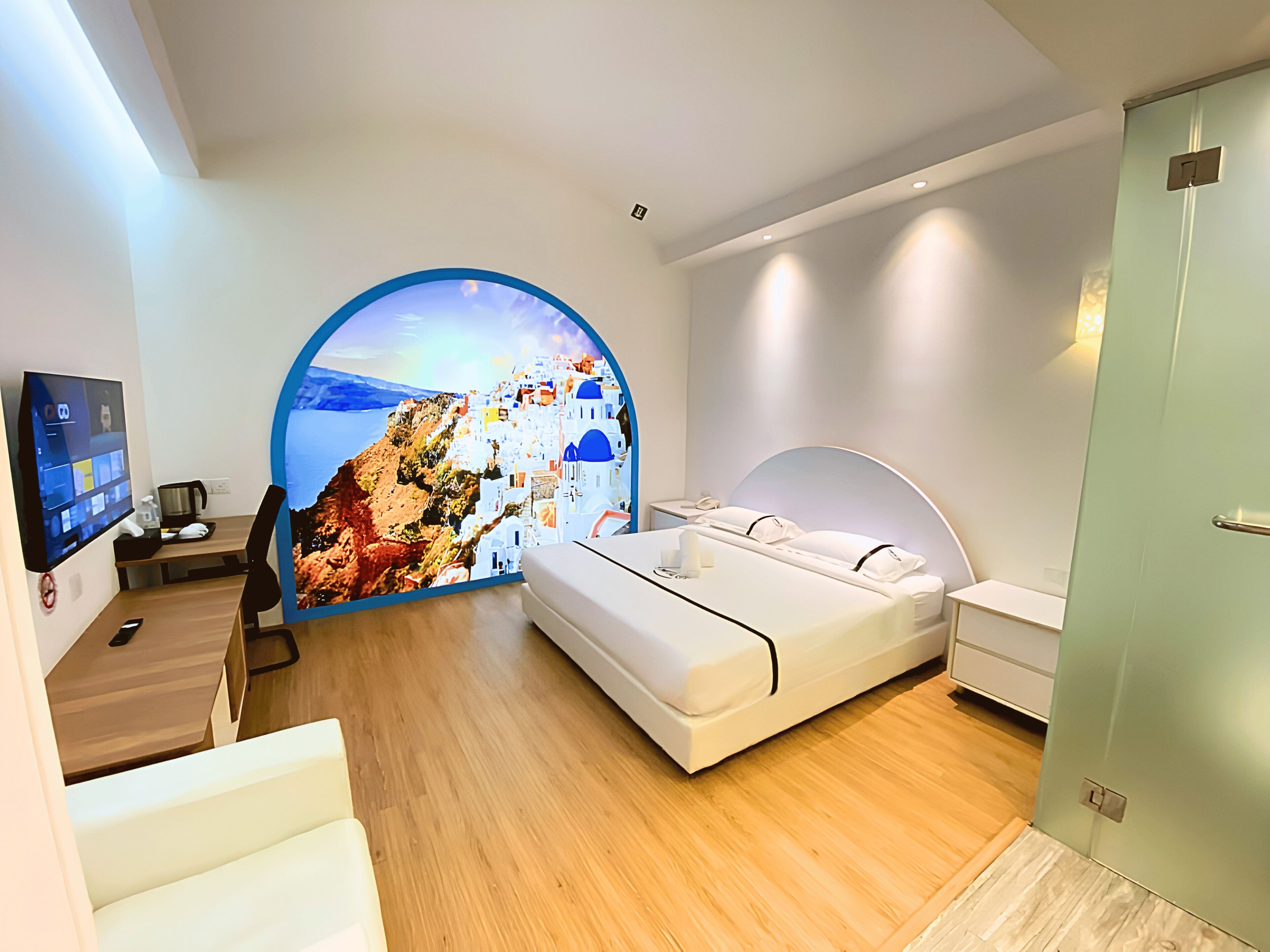 A modern hotel room with a bed, a desk, a chair, and a large circular window with a scenic view.