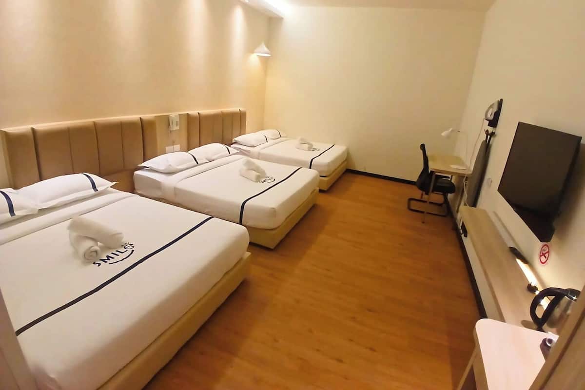 Ein Hotelzimmer mit drei Betten, einem Fernseher, einem Schreibtisch und einem Stuhl.