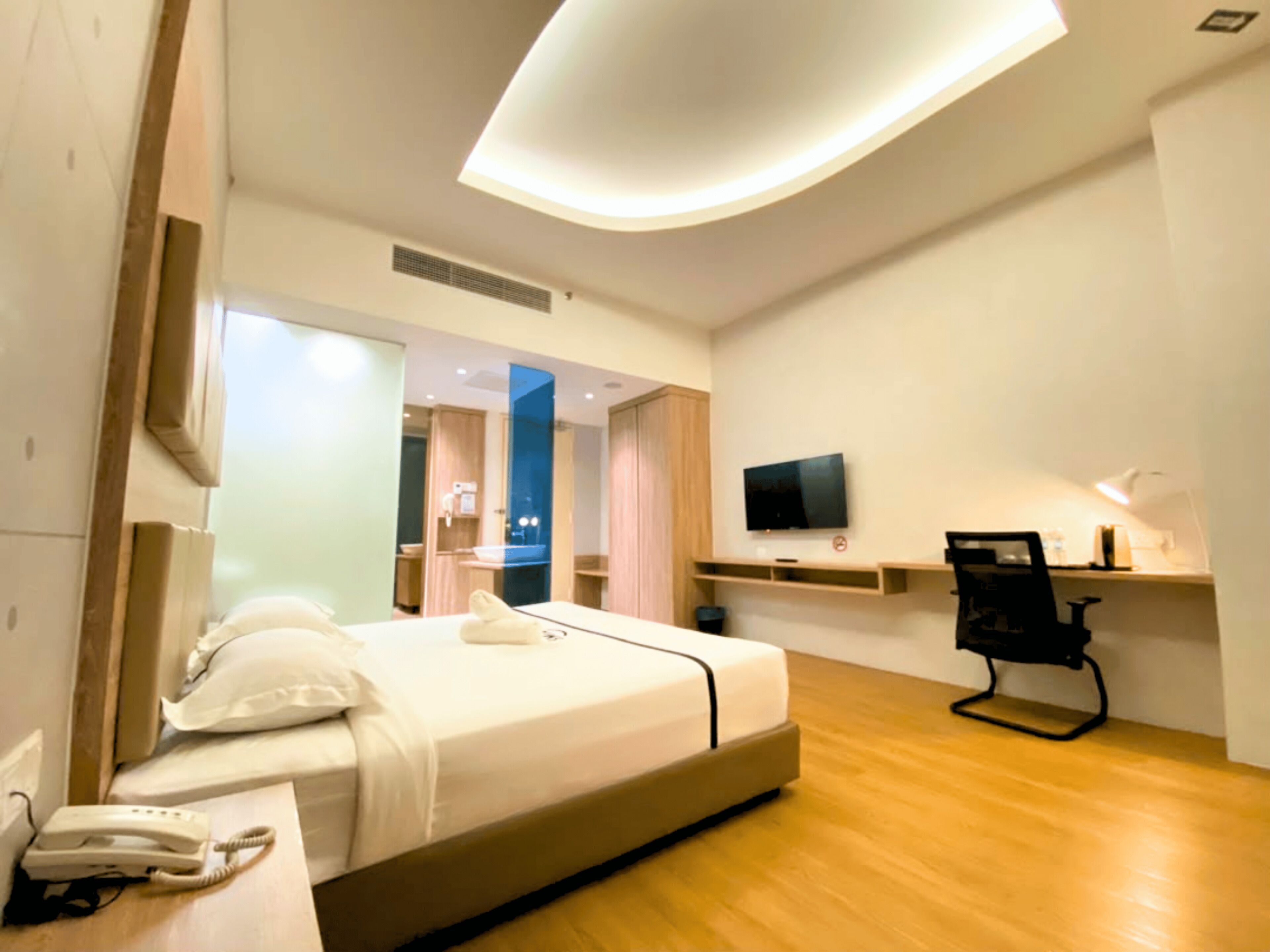 Habitación de hotel con cama, teléfono junto a la cama, televisor, escritorio, silla y espejo.