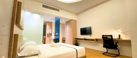 Habitación de hotel con cama, teléfono junto a la cama, televisor, escritorio, silla y espejo.