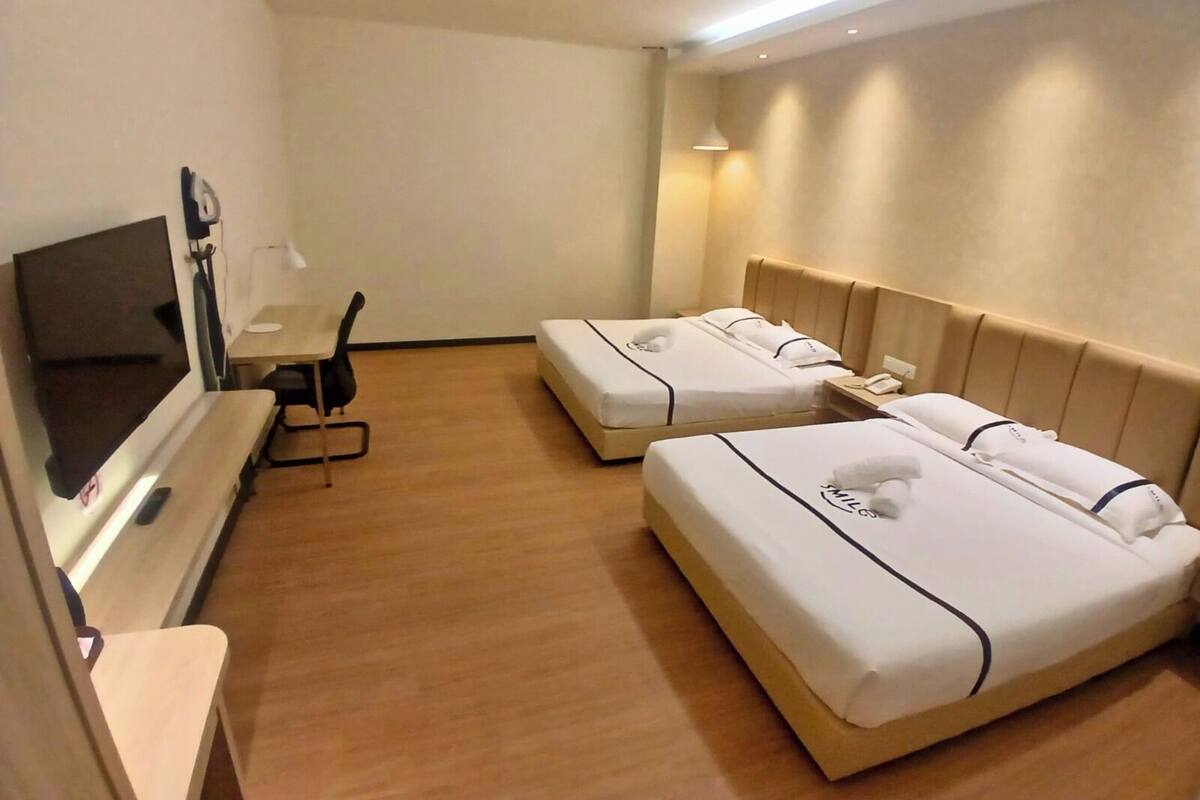 Ein Hotelzimmer mit zwei Betten, einem Schreibtisch, einem Fernseher und einer Lampe.