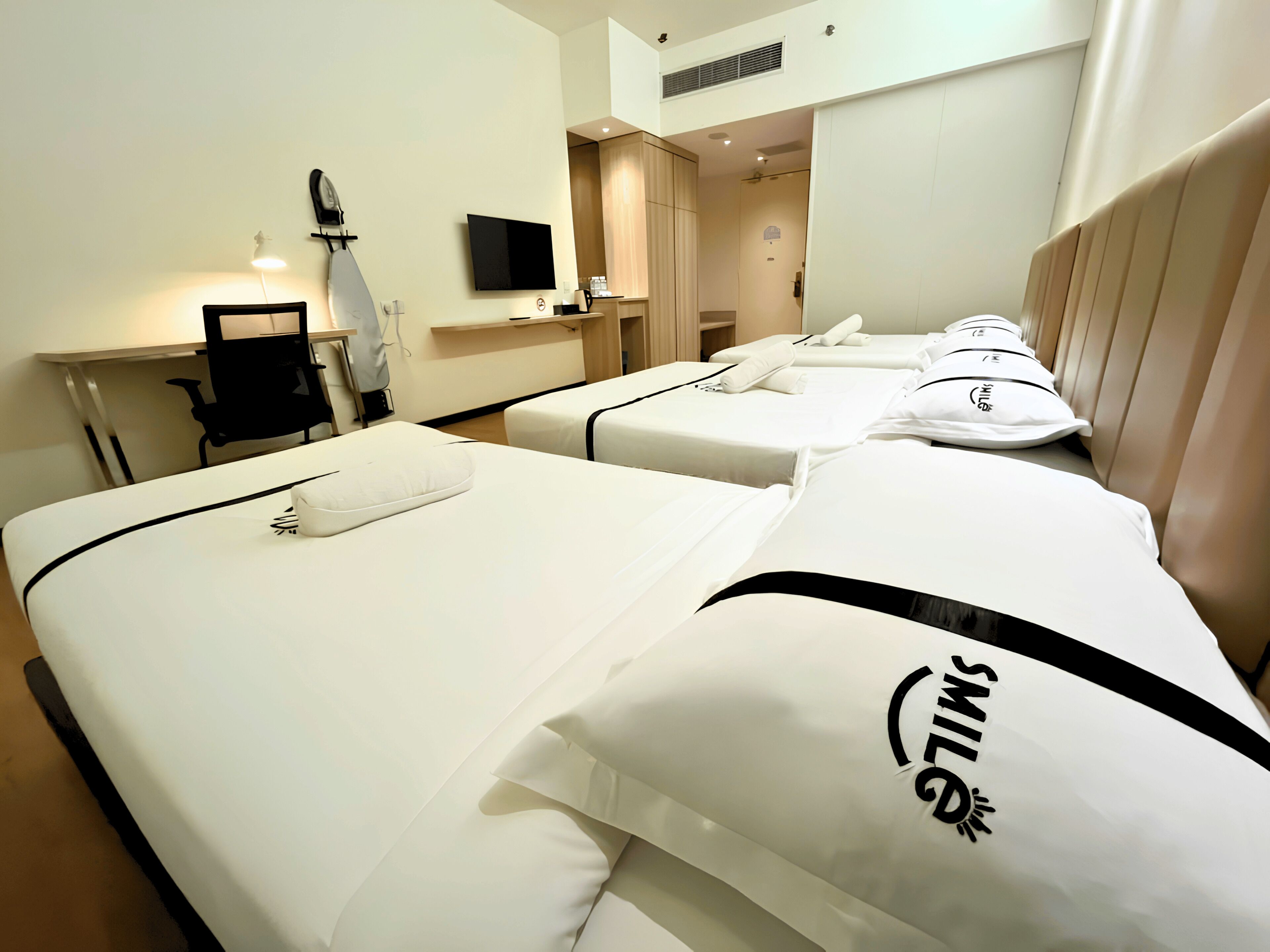 Habitación de hotel con dos camas, un escritorio, una silla, televisión y zona de ducha.