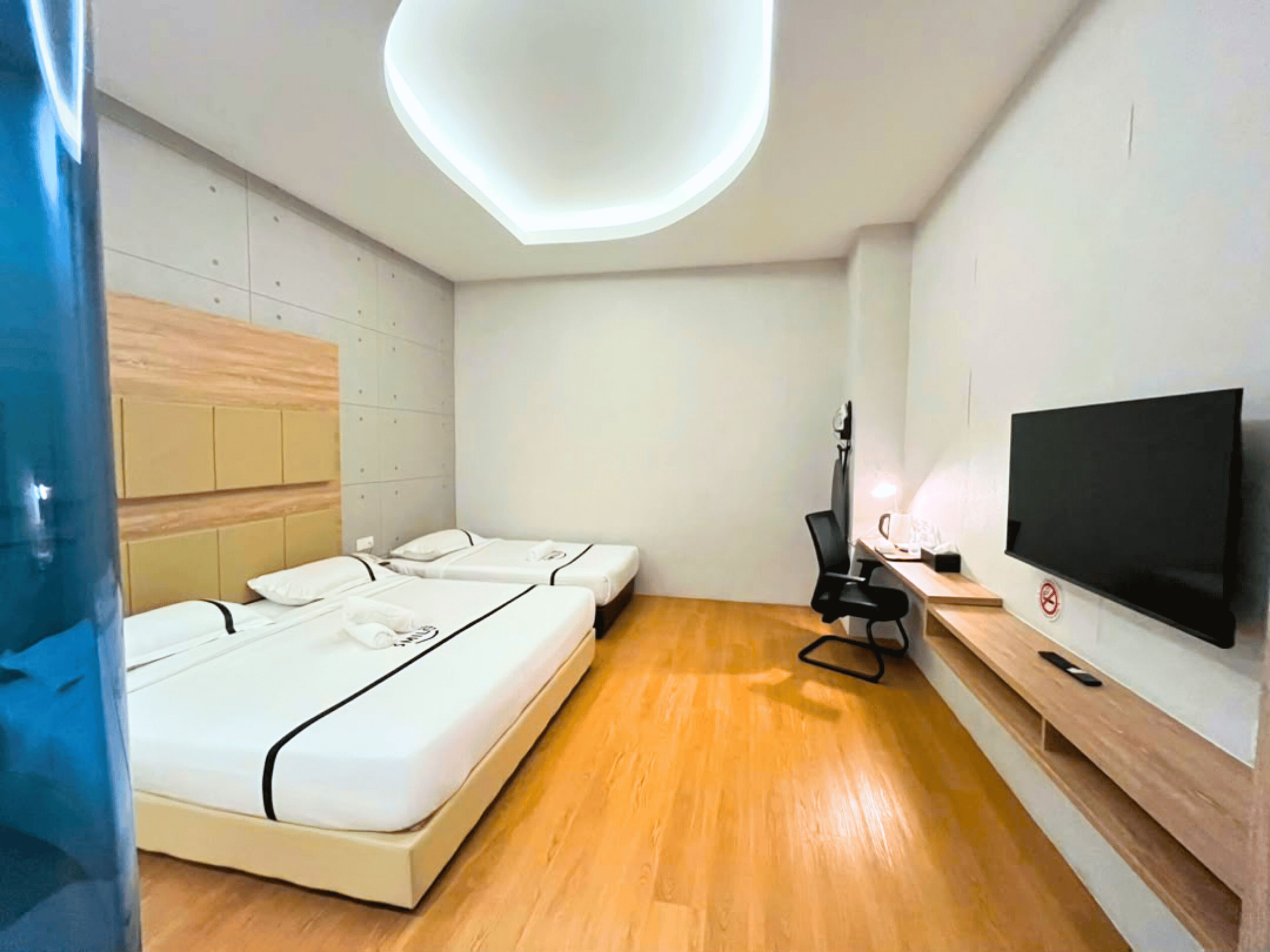 A modern hotel room with a large bed, a desk with a computer, a flat-screen TV, and a ceiling light fixture.