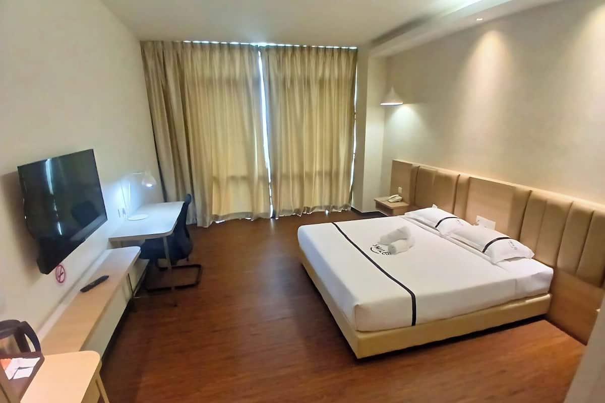 Ein Hotelzimmer mit Bett, Schreibtisch mit Stuhl, Fernseher und Nachttisch mit Telefon.