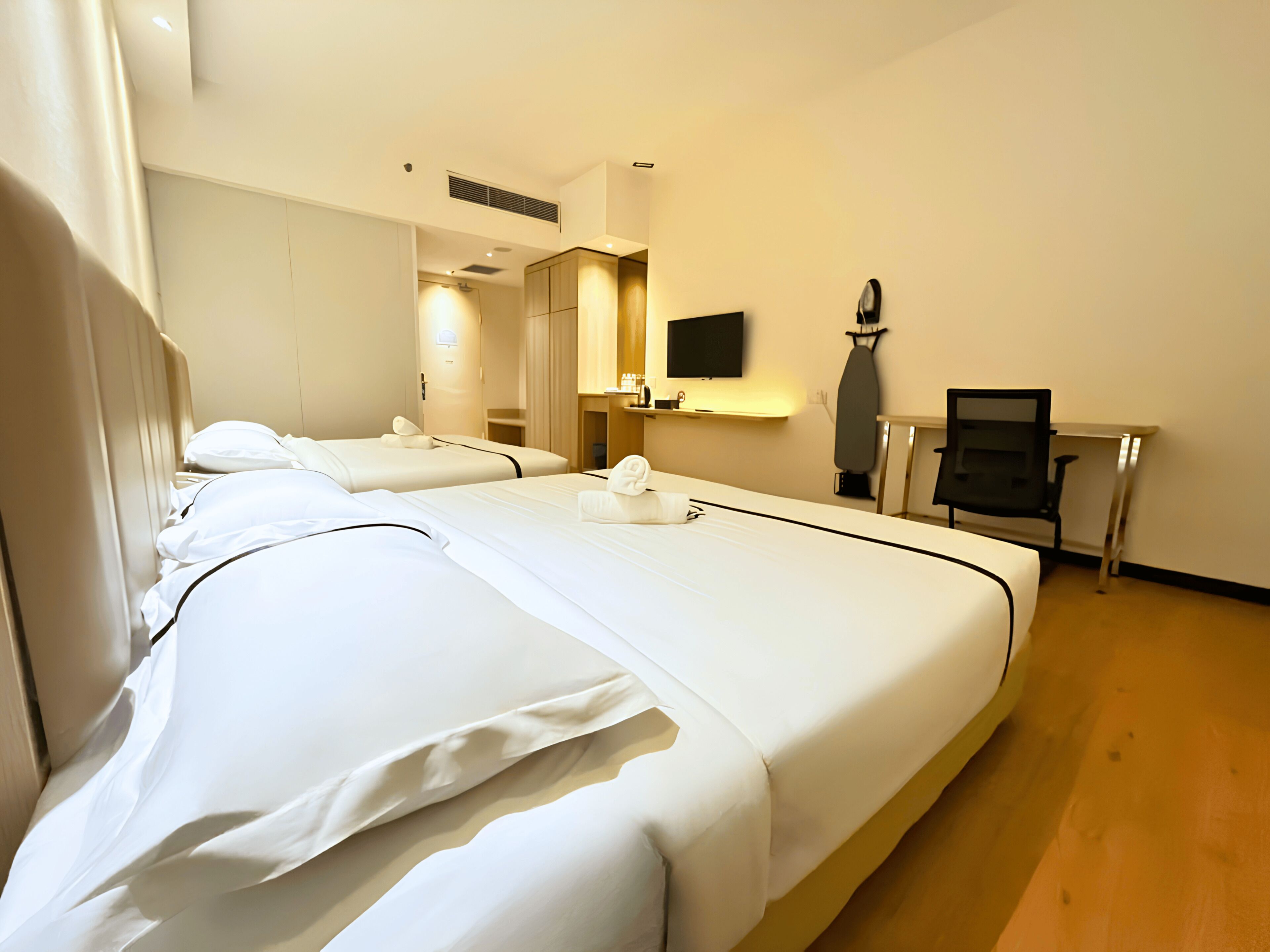 A hotel room with two beds, a flat-screen TV, an ironing board, and a desk.
