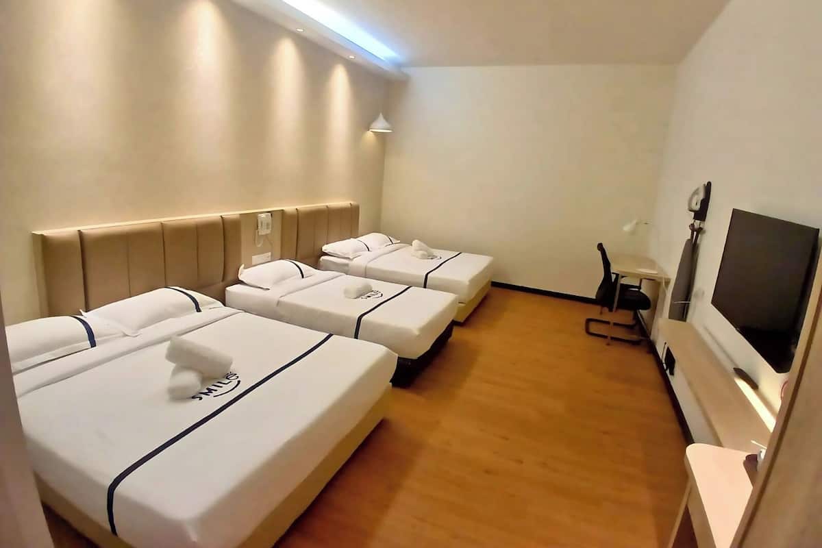 Ein Hotelzimmer mit drei Einzelbetten, einem kleinen Schreibtisch mit Stuhl und einem Fernseher.