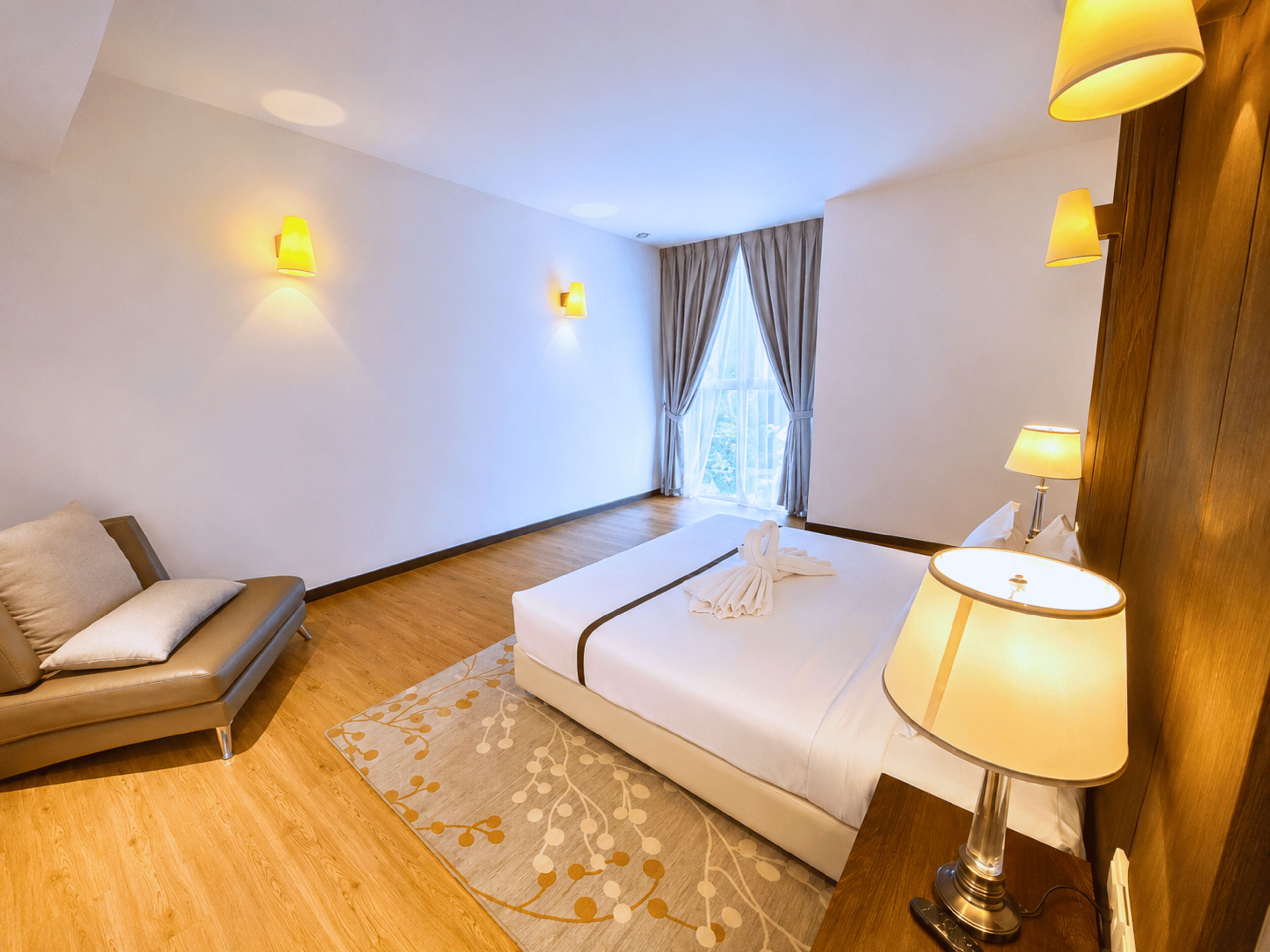 A hotel room with a bed, a sofa, a lamp, and a window with curtains.