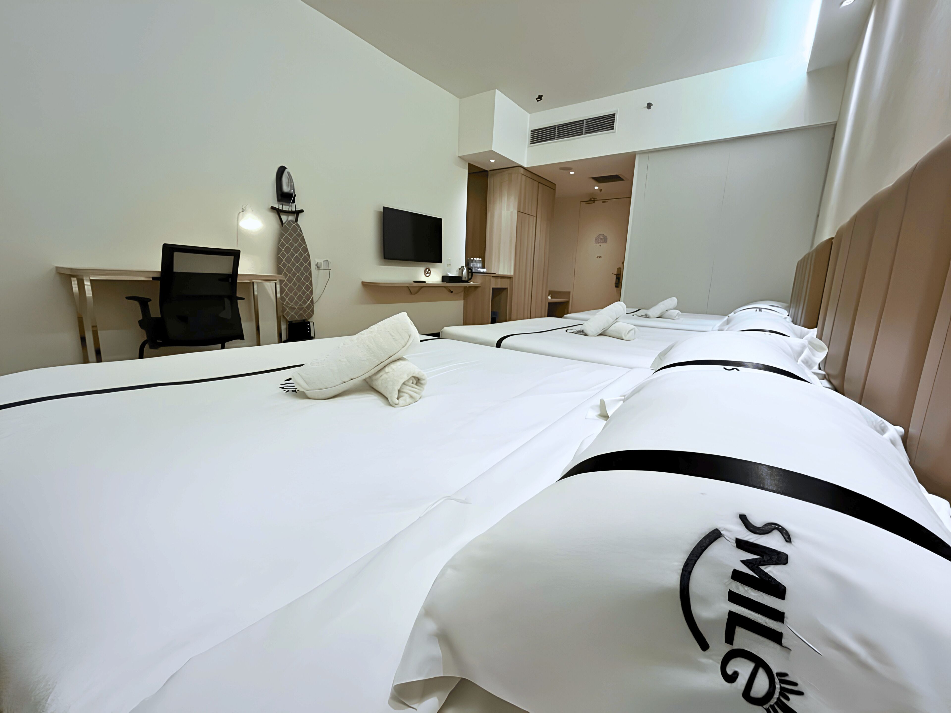 Hotelkamer met drie bedden, een bureau, een stoel, een flatscreen televisie en een spiegel.