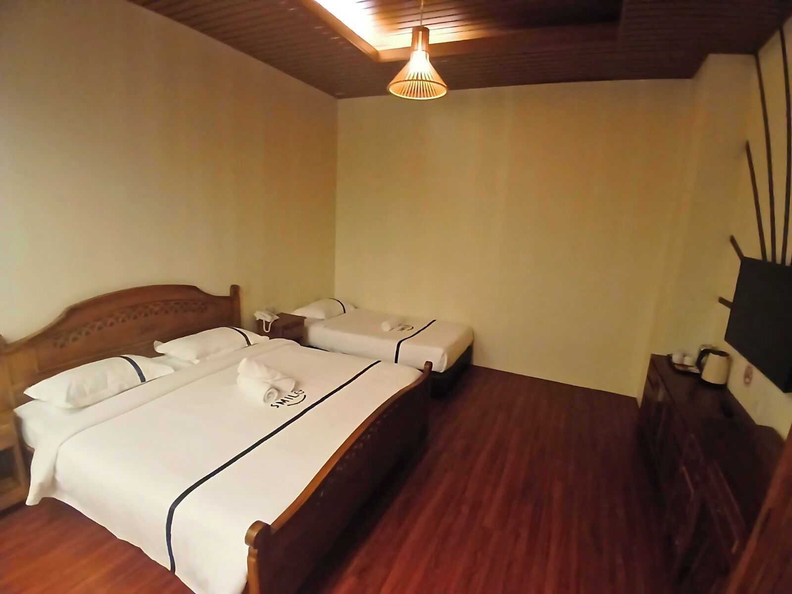A hotel room with a wooden bed, a bedside table, a nightstand, and a wall-mounted TV.