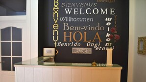 Un comptoir d’accueil avec un mur noir orné de panneaux d’accueil multilingues, affichant le mot « BIENVENUE » dans différentes langues.