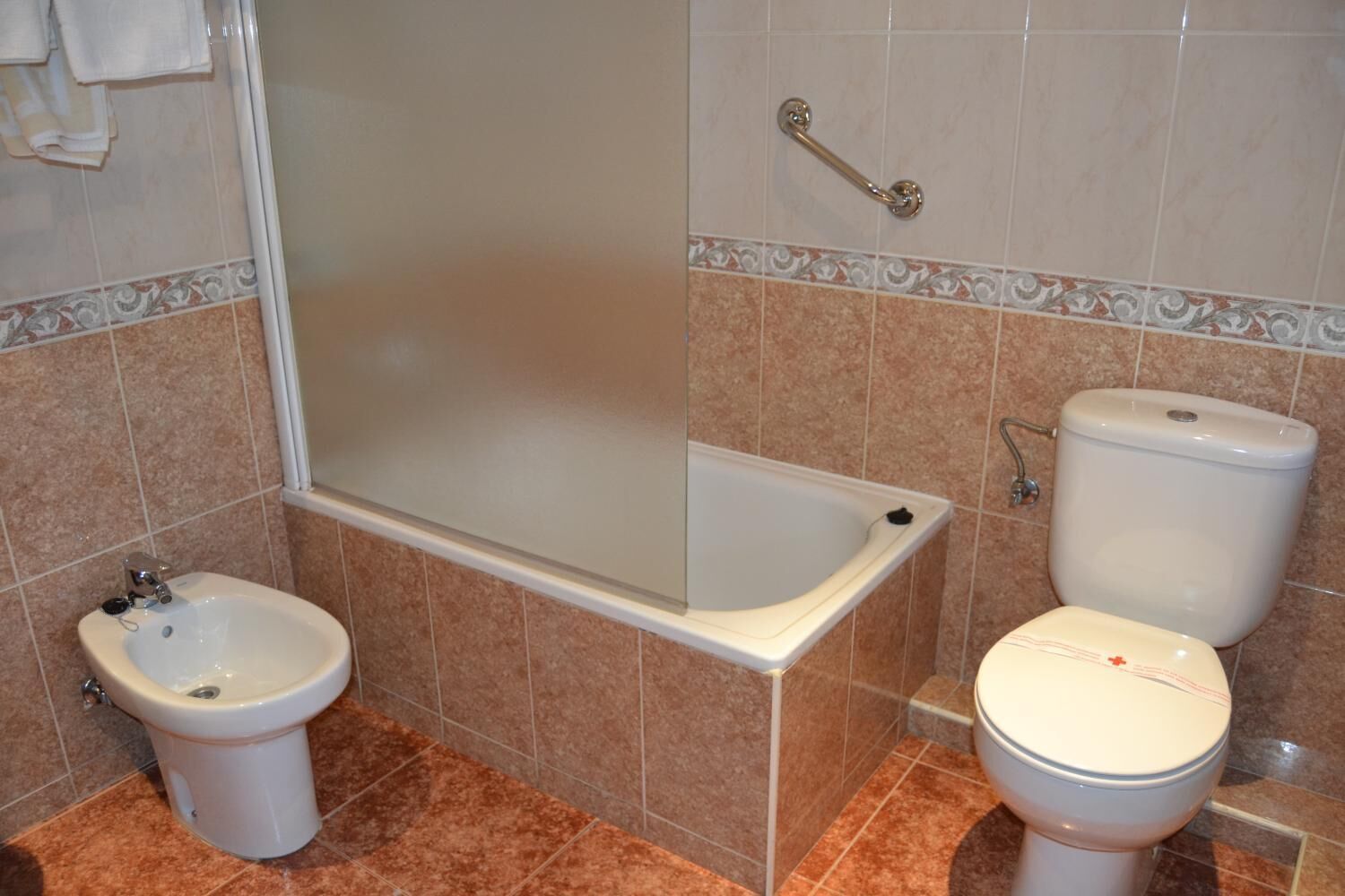 A bathroom with a bathtub, bidet, toilet, and a handrail.