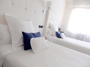 Een hotelkamer met twee bedden, witte beddengoed en een nachtkastje met een lamp.