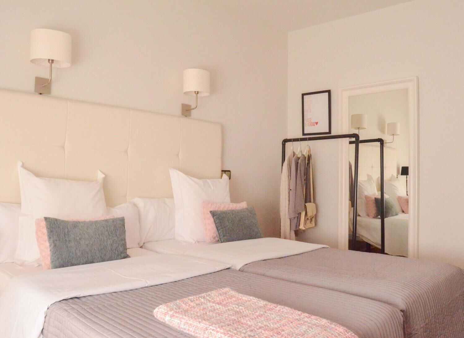 A double bed with a headboard, two bedside lamps, a mirror, and a clothing rack.