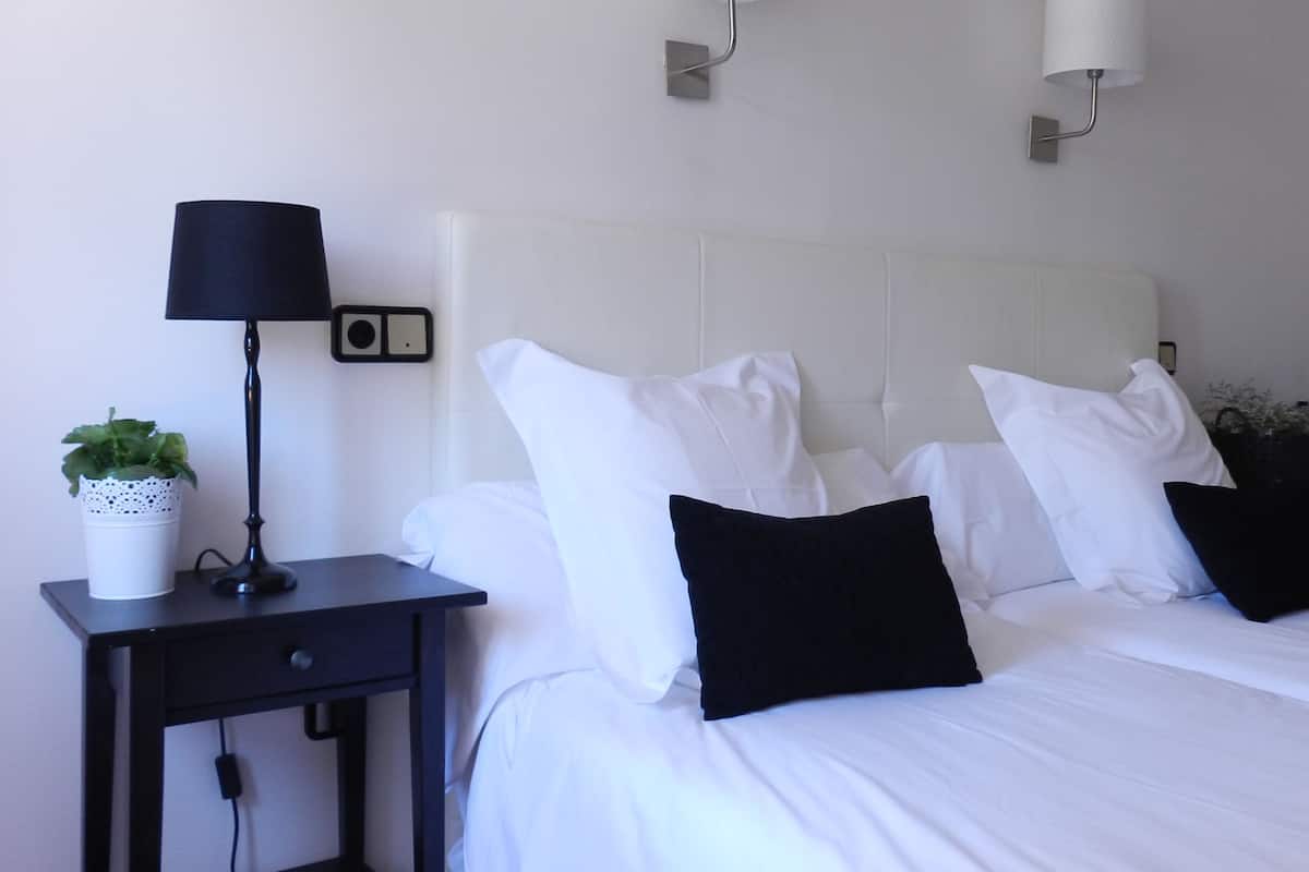 Ett hotellrum med en säng, två sänglampor, ett nattduksbord med en lampa och en växt, samt ett vägguttag.