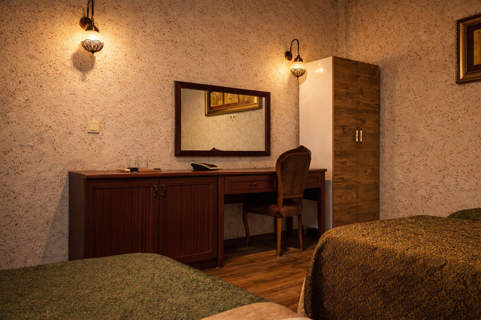 A room with a wooden desk, a chair, a bed, and two wall-mounted lights.