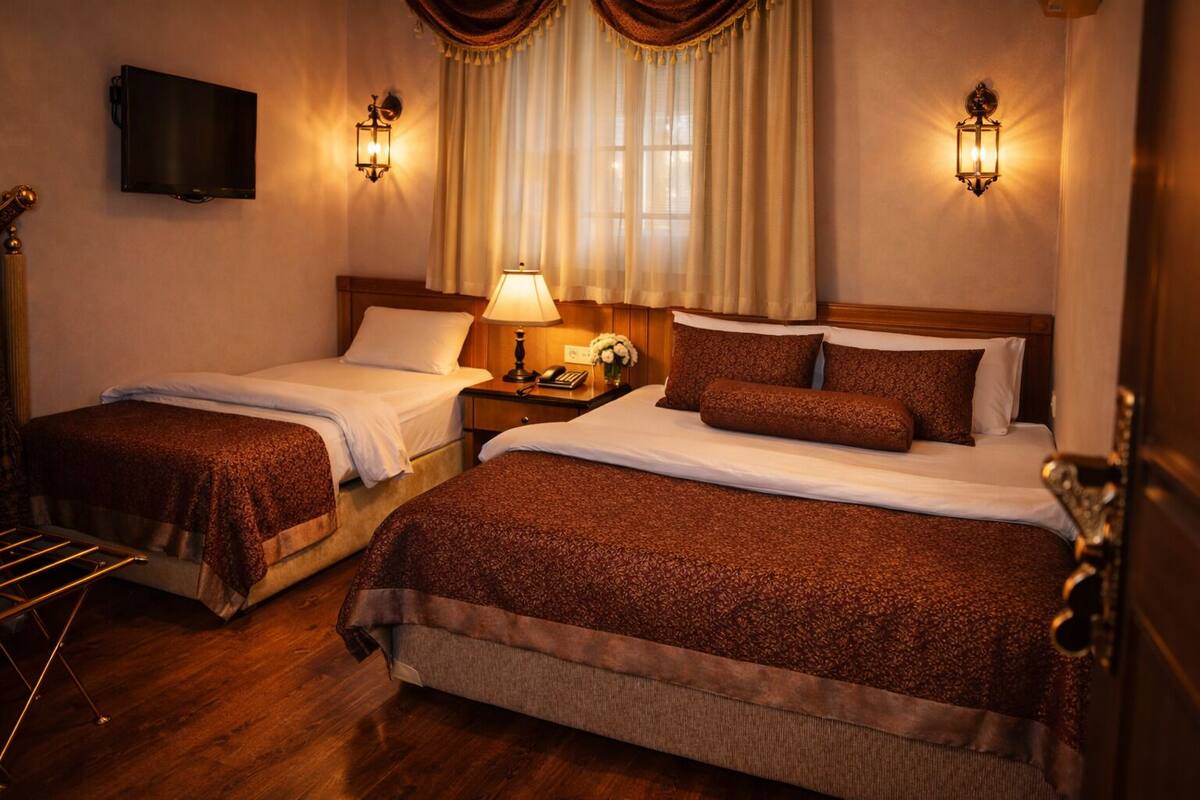 A hotel room with two single beds, a wooden floor, a flat-screen TV, and wall-mounted lamps.