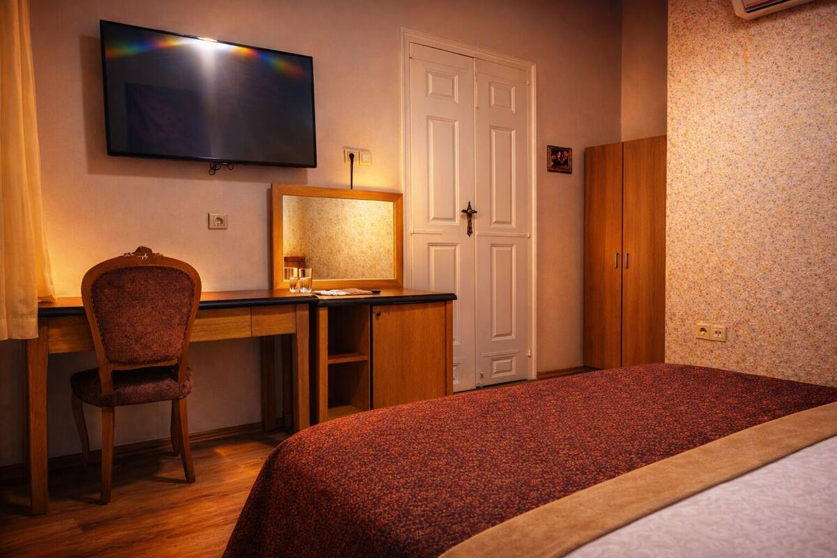 A hotel room with a bed, a desk with a chair, a television, and a wardrobe.