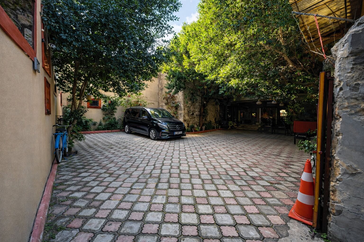 Un patio empedrado con un coche estacionado, una bicicleta y un cono de tráfico.