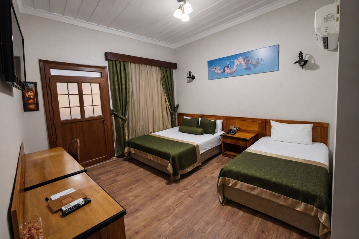 A hotel room with two beds, a wooden desk, a telephone, and a painting on the wall.