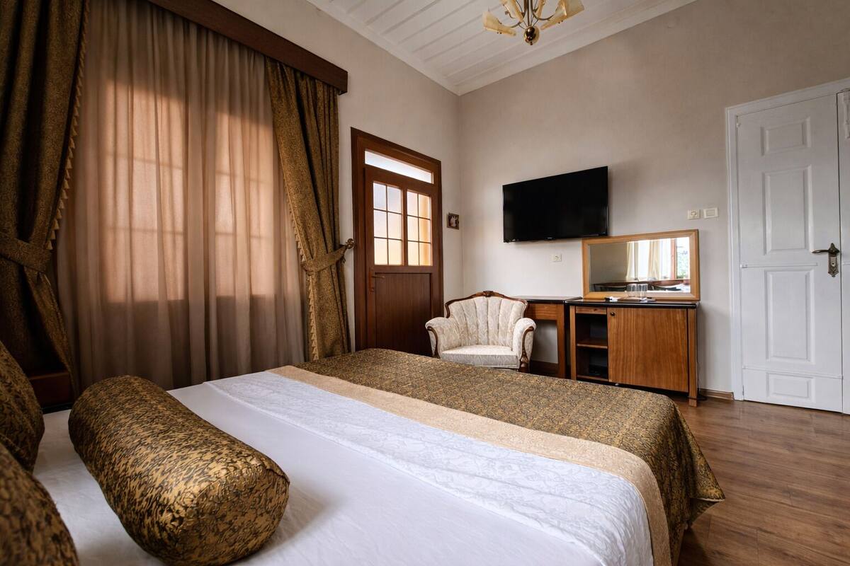 A hotel room with a large bed, a desk with a mirror, a television, and a wardrobe.
