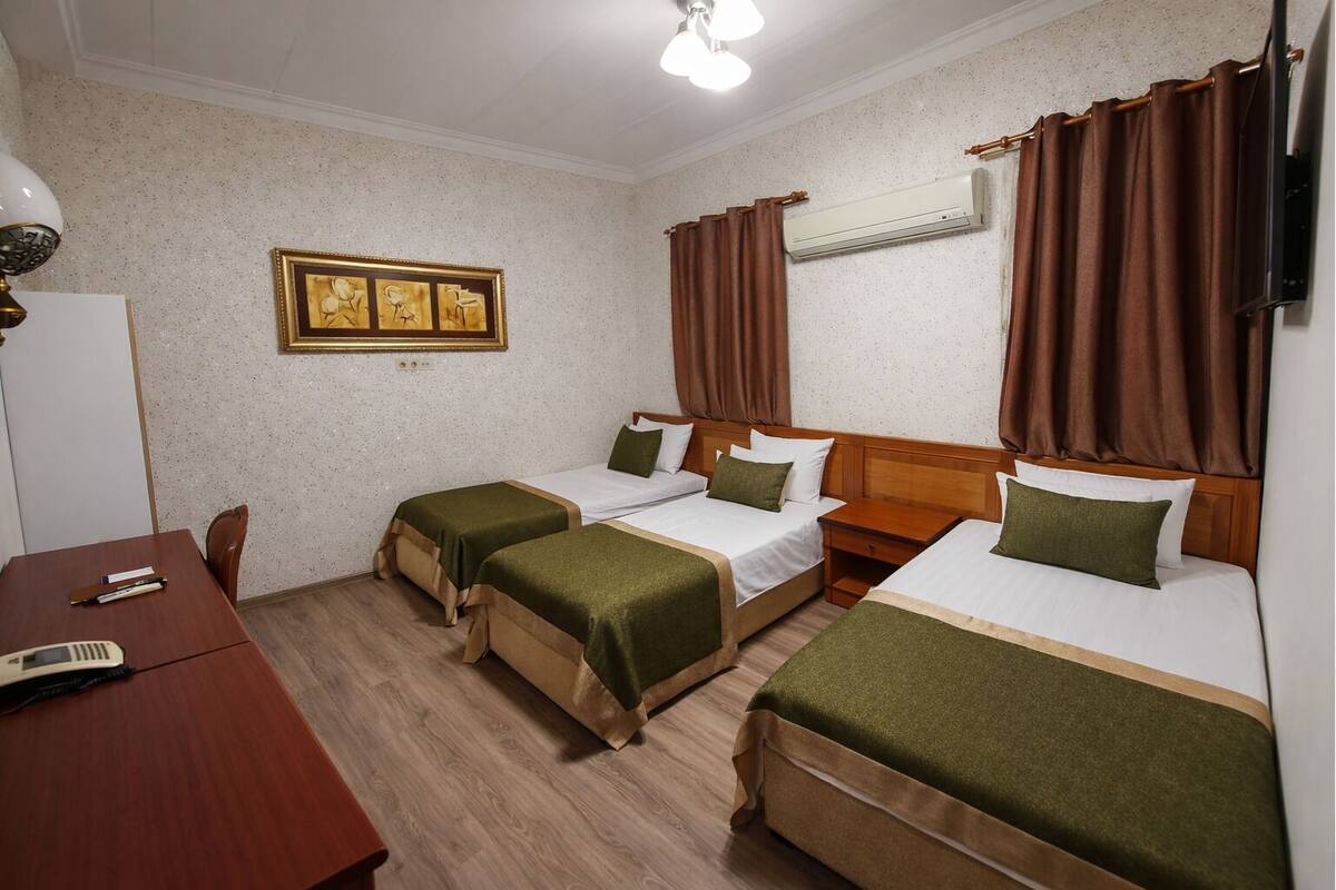 A hotel room with two single beds, a wooden desk, a chair, a framed picture on the wall, and an air conditioning unit.