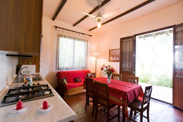 Una cocina acogedora con estufa a gas, un sofá rojo y una mesa de comedor lista para cuatro comensales.