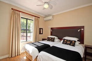 A hotel room with two beds, a ceiling fan, an air conditioning unit, and a window with curtains. - Vilaroux (Stellenbosch)