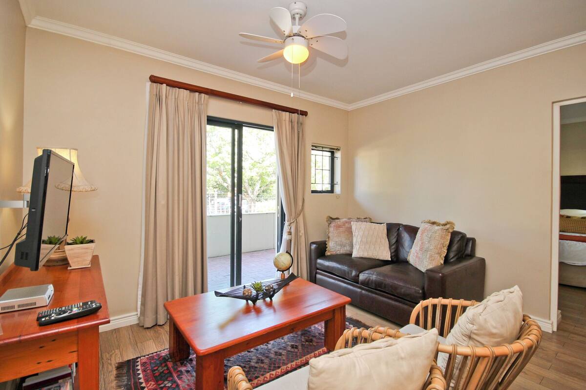 A living room with a leather sofa, a wooden coffee table, a wicker chair, a television, and a ceiling fan.