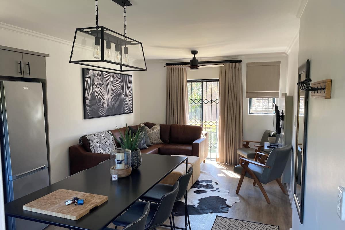 A modern living room with a dining area, a sofa, a coffee table, and a large window with curtains.