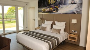 A modern hotel room with a large bed, a painting of a racing car, and a sliding glass door to the outside. - Résidence des Pilotes (Le Vigeant)