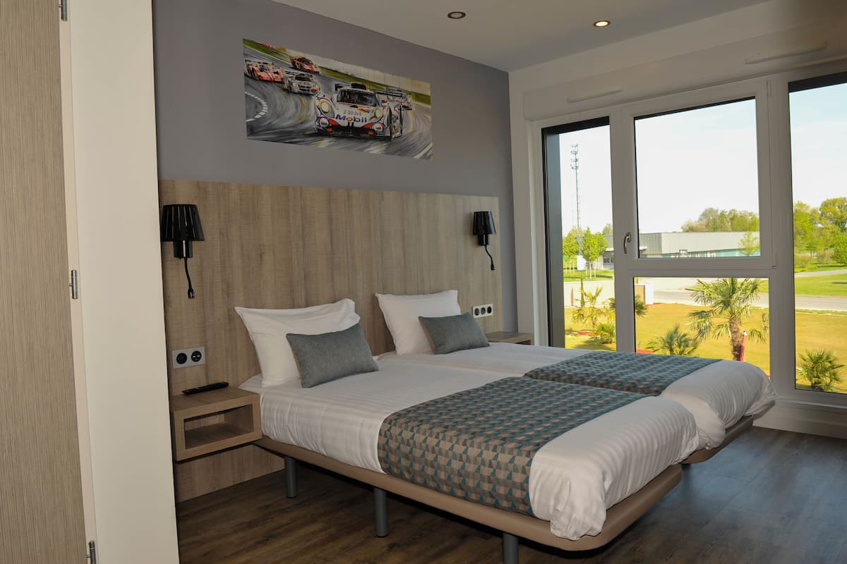 A modern hotel room with two beds, a large window with a view of a golf course, and a wall-mounted painting of a racing car.