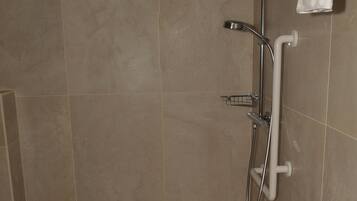 A shower area with a handheld showerhead, a wall-mounted towel rack, and a tiled floor.