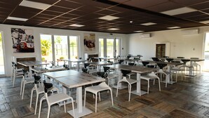 A spacious dining area with multiple tables and chairs, large windows, and artwork on the walls. - Résidence des Pilotes (Le Vigeant)