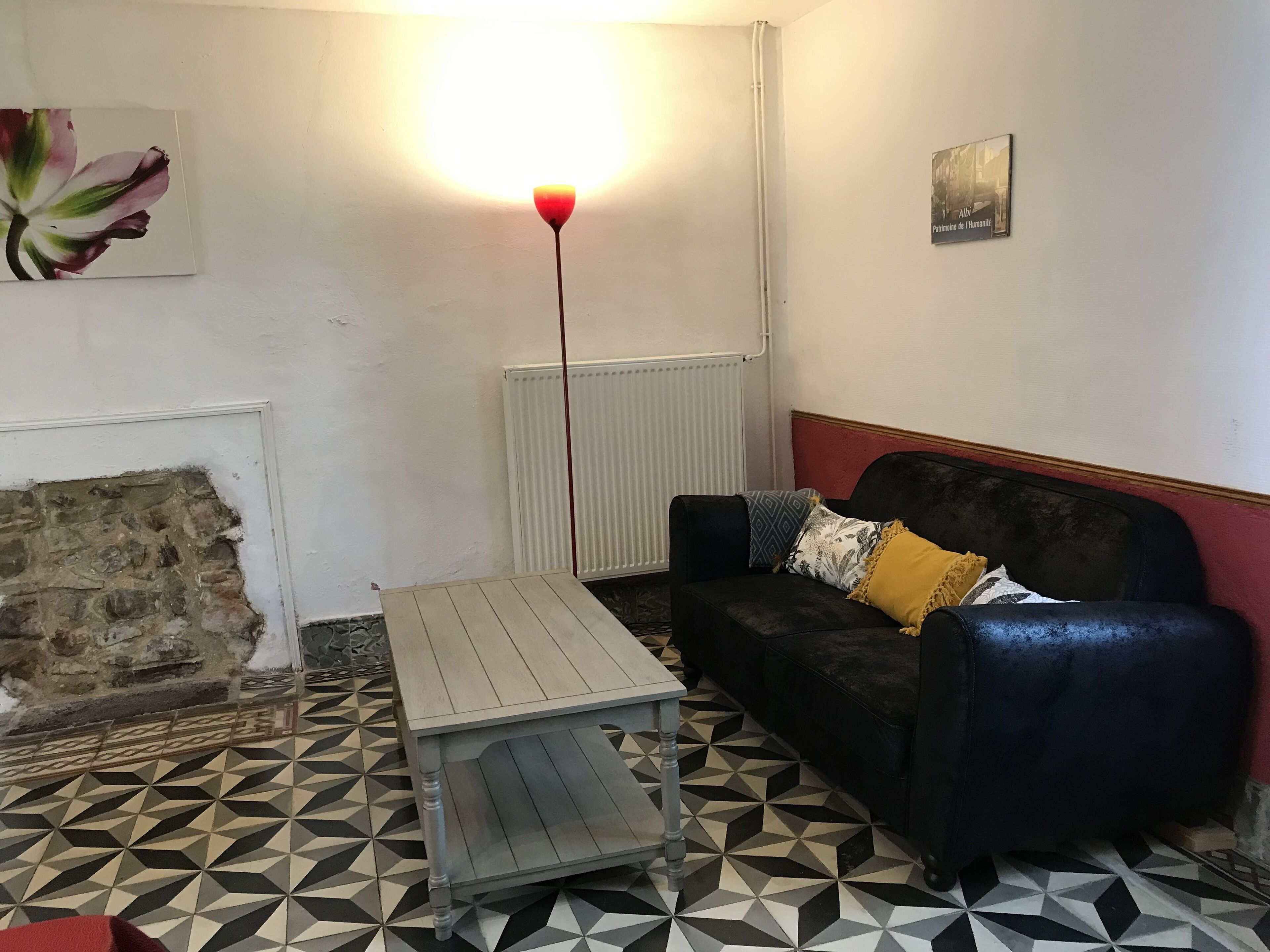 Un salon avec un canapé en cuir noir, une table basse en bois, un sol à motifs, un radiateur et un tableau accroché au mur.