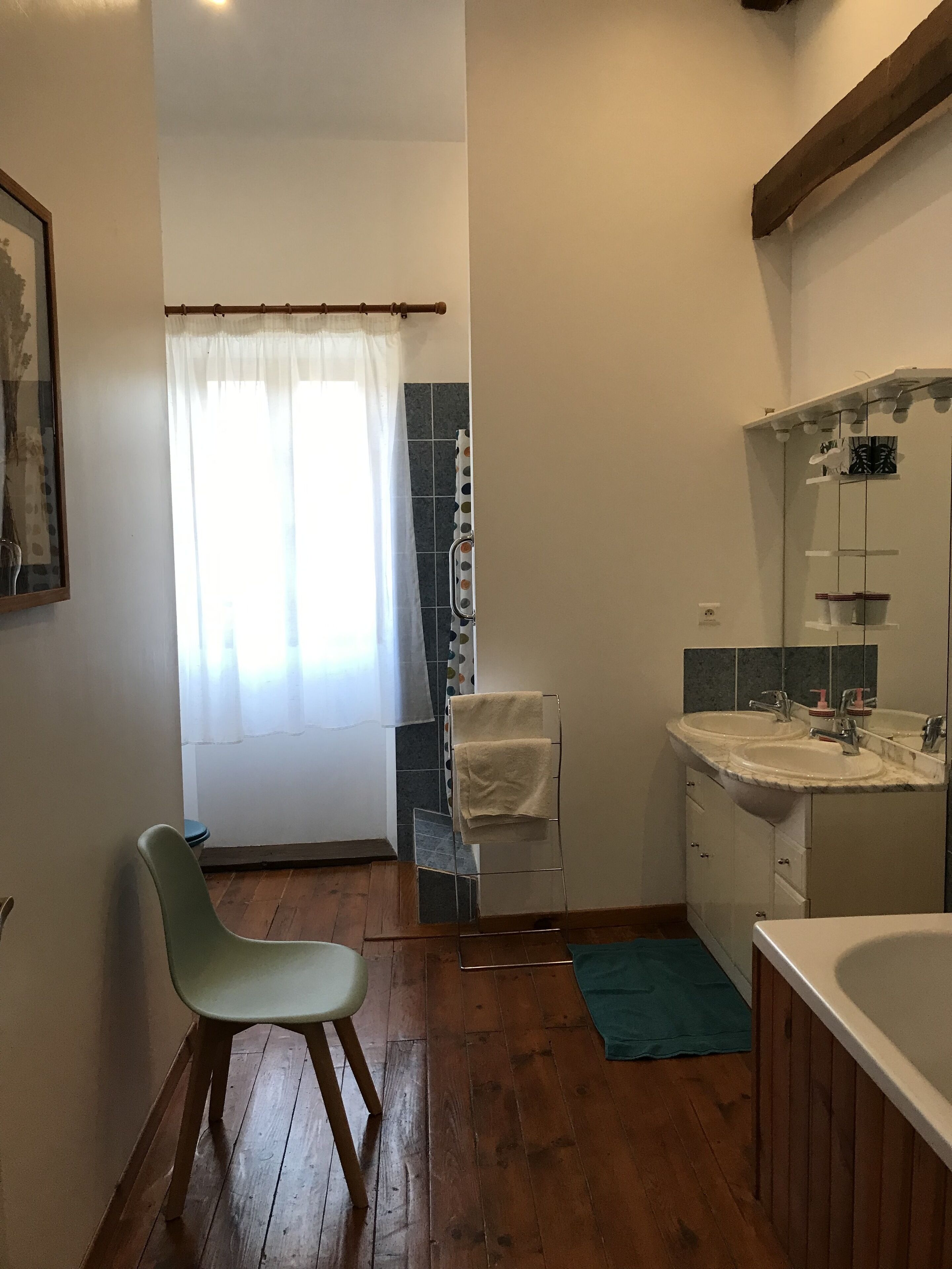 Une salle de bain avec un plancher en bois, une douche avec un rideau, un lavabo avec un miroir et une chaise.