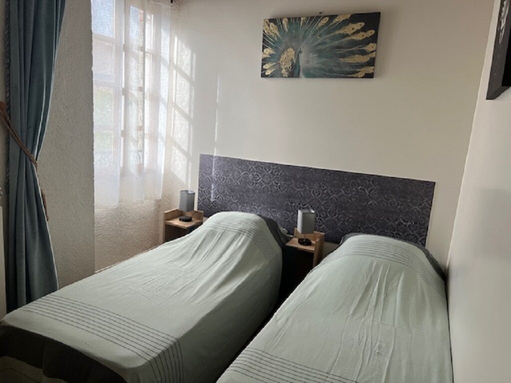 Habitación de hotel con dos camas individuales, una mesita de noche con lámpara, un adorno en la pared y una ventana con cortinas.