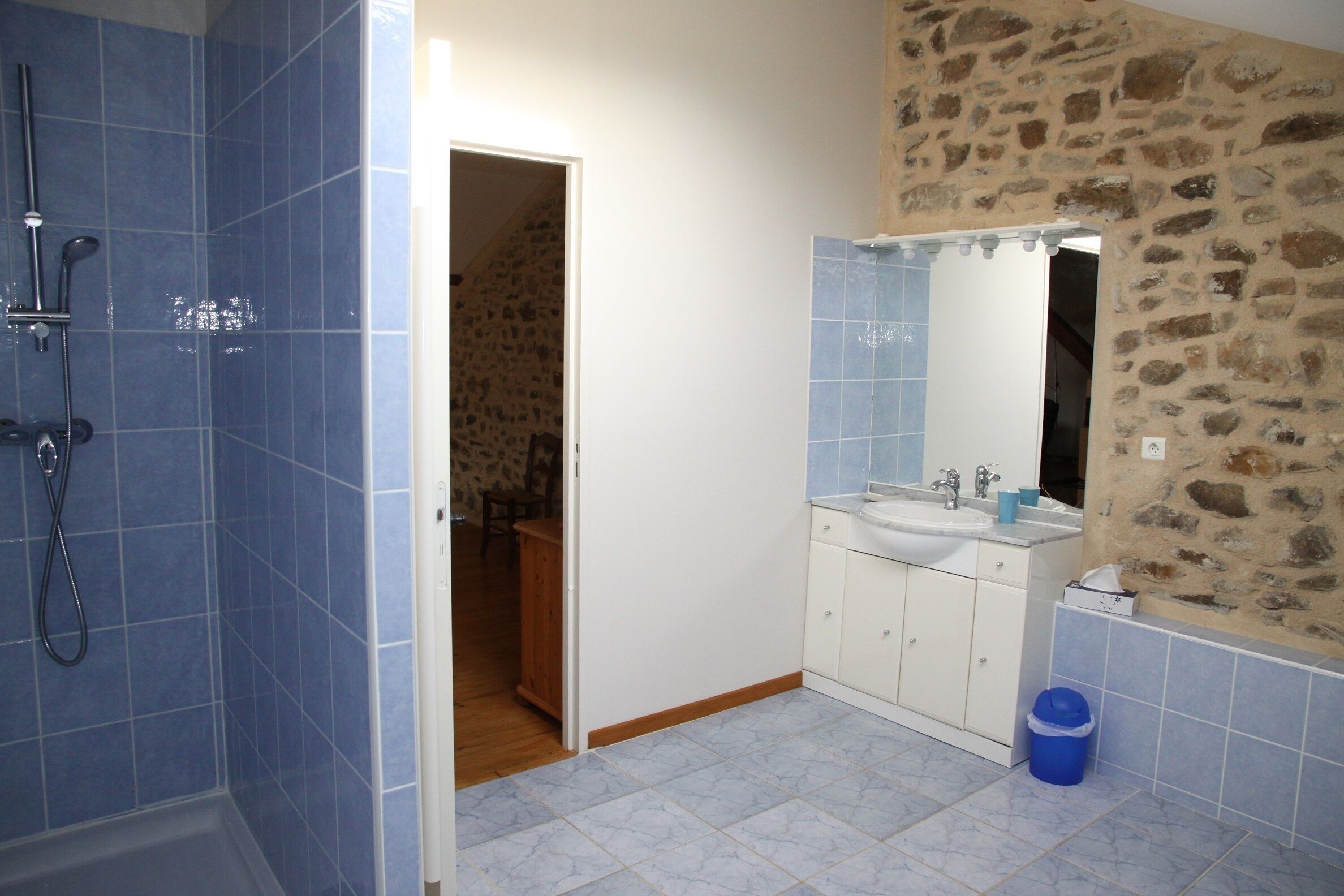 A bathroom with blue tiles, a stone wall, a sink, and a shower.