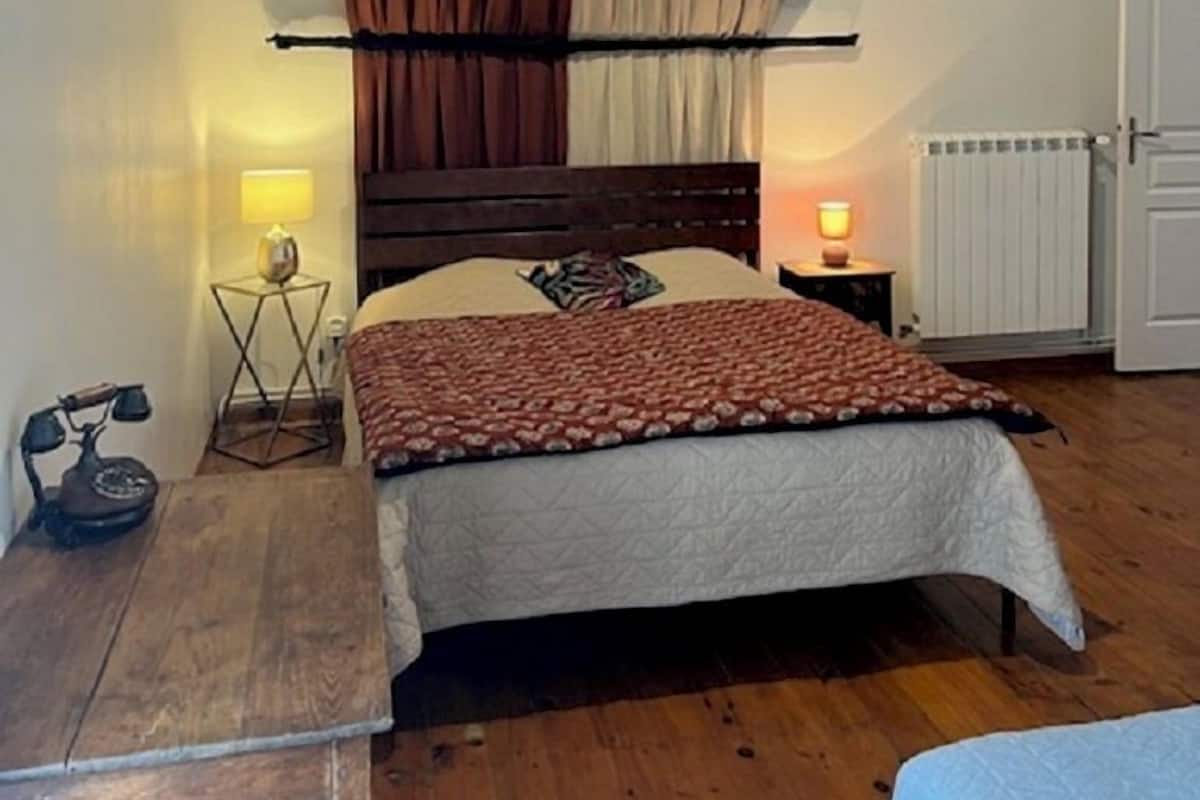 A bedroom with a wooden bed, a nightstand with a lamp, a radiator, and a wooden bench.
