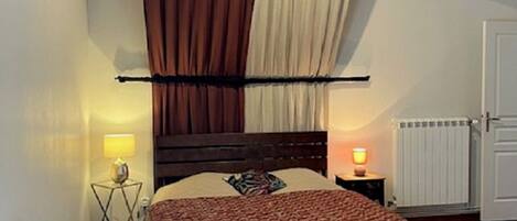 Une chambre avec un lit en bois, une table de chevet avec une lampe, un radiateur et un banc en bois.