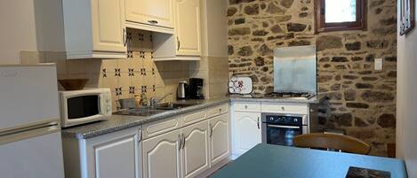 A kitchen with white cabinets, a microwave, a stove, and a sink. There is a stone wall and a window with a view of the outdoors.