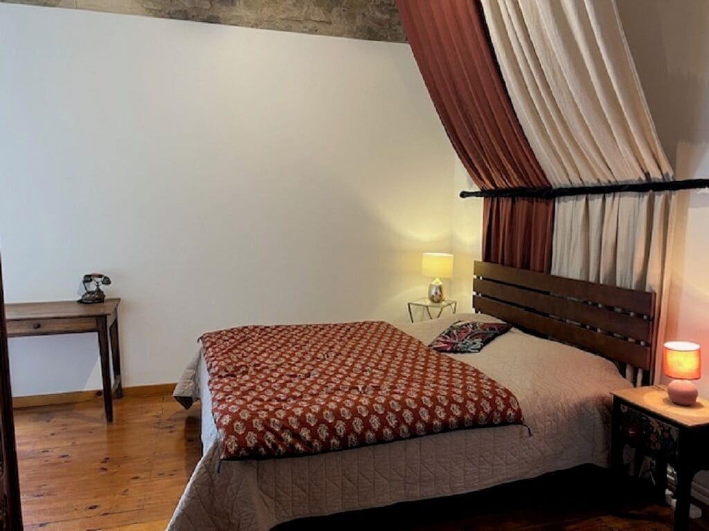 Een slaapkamer met een bed, nachtkastje, lamp en raam met gordijnen.