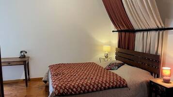 Een slaapkamer met een bed, nachtkastje, lamp en raam met gordijnen.