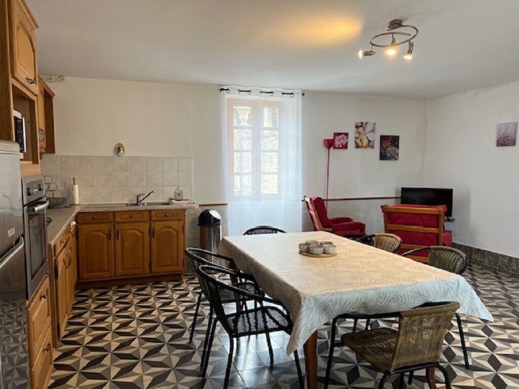 Una cocina con comedor, que cuenta con piso de baldosas, armarios de madera, una mesa con sillas y una ventana con cortinas.