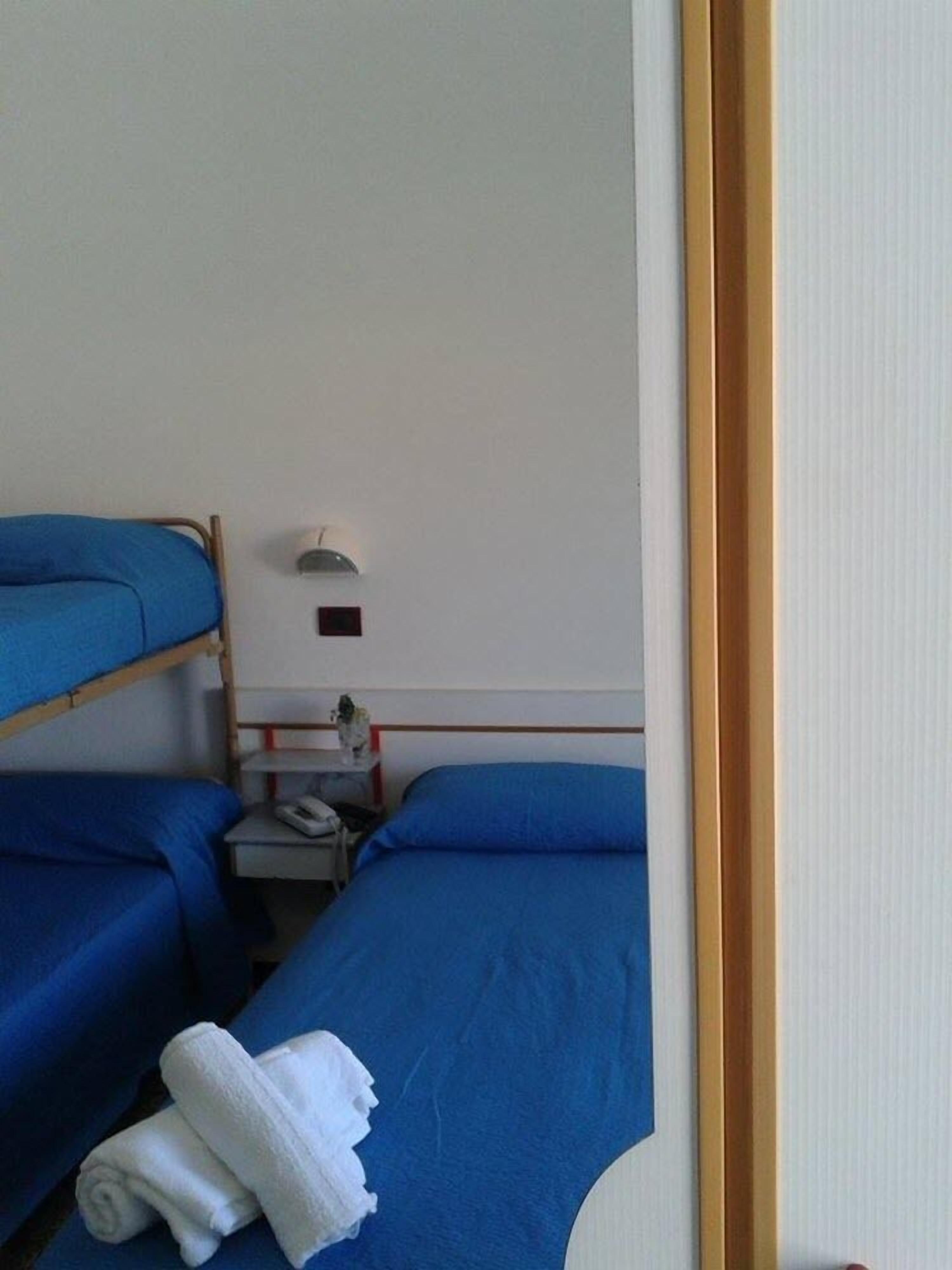 A room with bunk beds, a bedside table with a lamp, and a rolled-up towel on the floor.