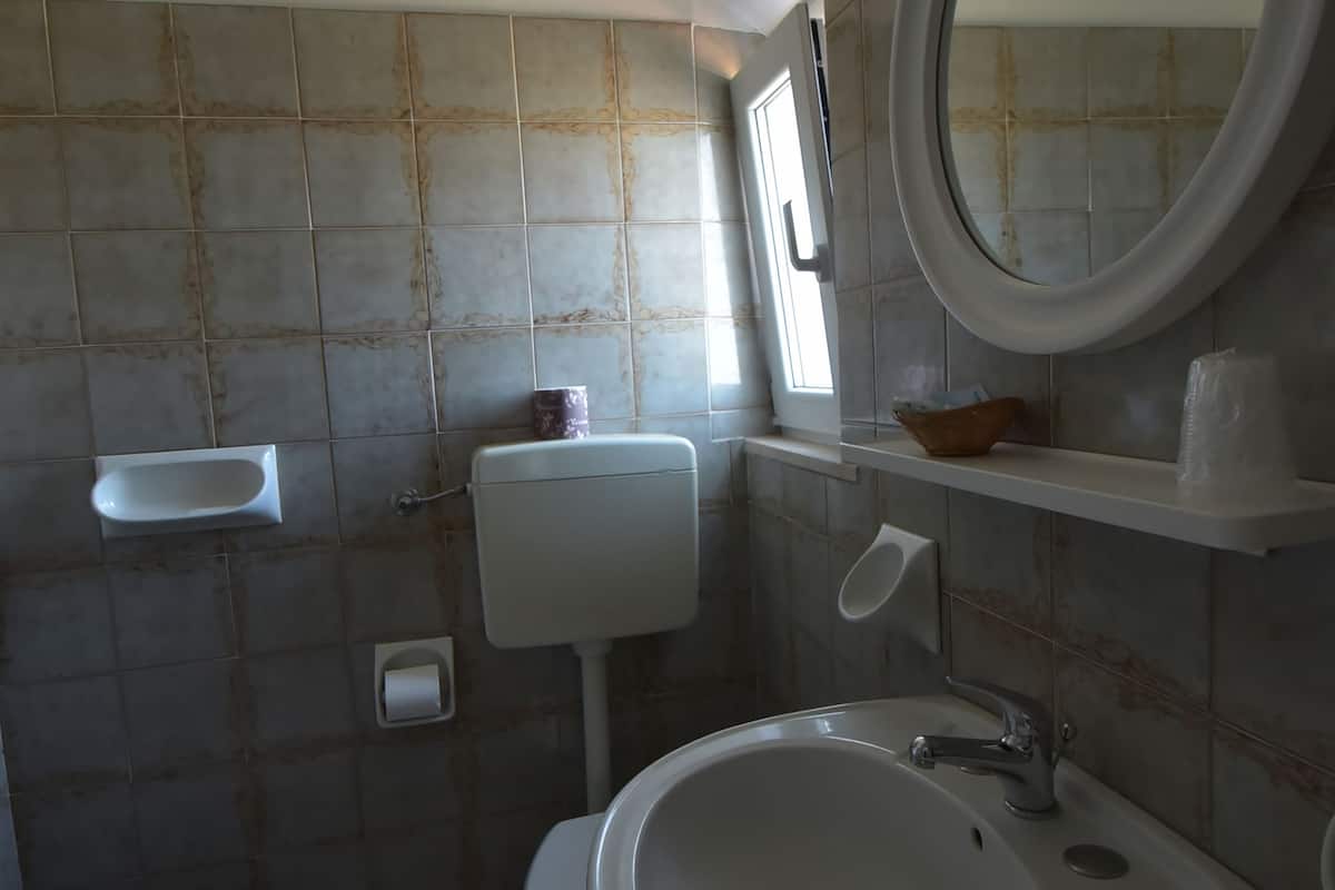 Un baño con inodoro, lavamanos y un pequeño estante con artículos de aseo.