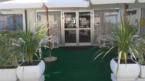 A building with a green artificial turf entrance, white potted plants, and a glass door leading inside. - Hotel Goya (Rimini)