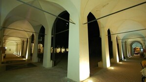 Ein Korridor mit gewölbter Decke und einem Ziegelboden, der zu einem entfernten, beleuchteten Bereich führt.