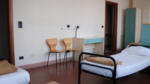 Ein Zimmer mit einem Einzelbett, einem Schreibtisch, zwei Stühlen, einem Kleiderschrank und einer Badezimmertür.