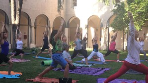 Eine Gruppe von Menschen praktiziert Yoga in einem Innenhof mit Bögen und Bäumen.