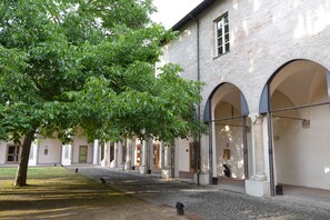 Une cour intérieure avec un bâtiment doté d’arcades et d’un arbre qui offre de l’ombre.